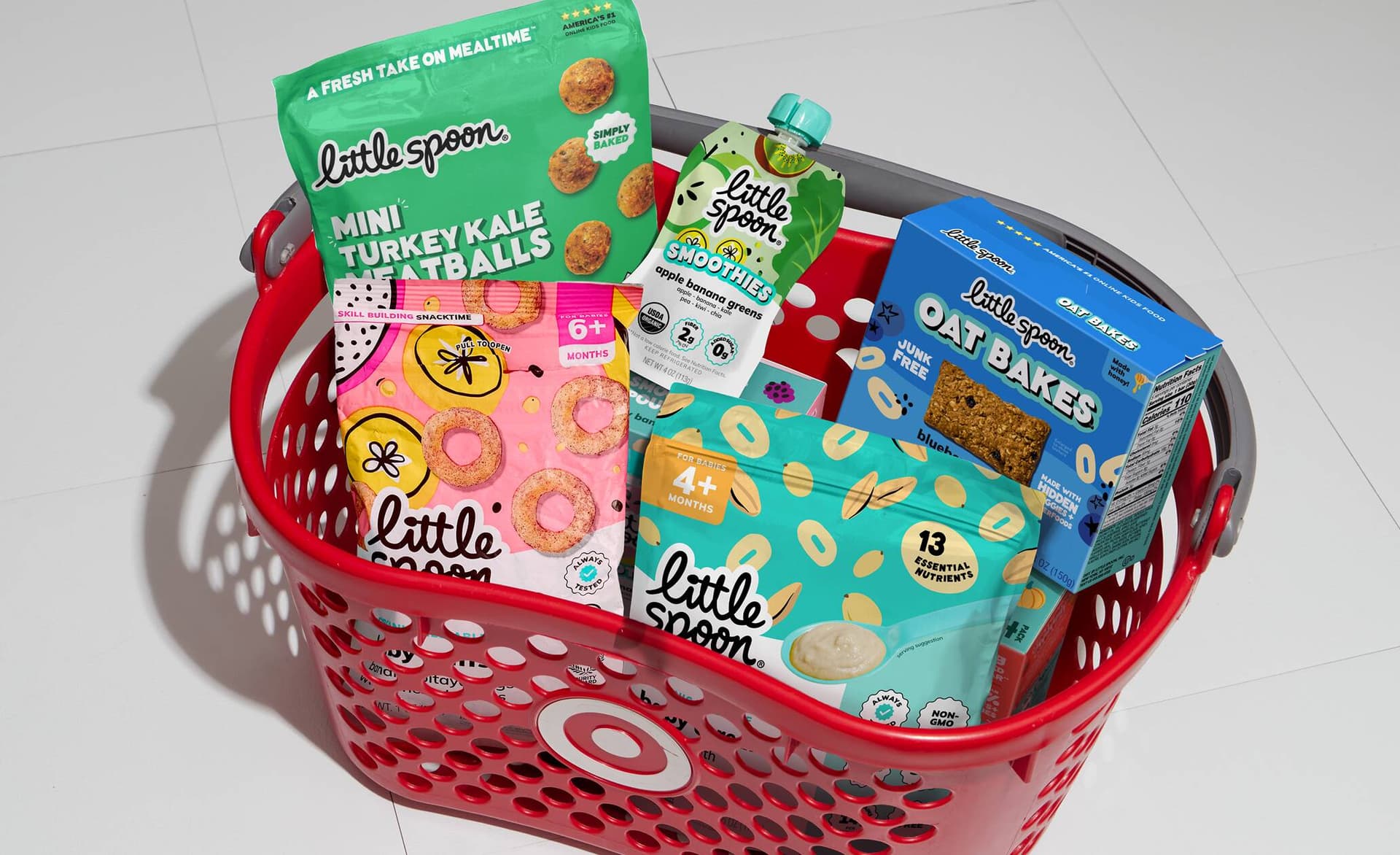 Red Target shopping basket filled with Little Spoon products, including Mini Turkey Kale Meatballs, a Smoothies pouch, Oat Bakes, and snacks.